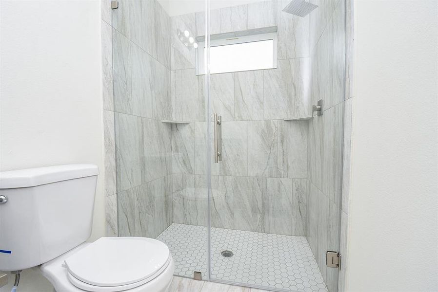 Modern bathroom with marble tiles, glass shower enclosure, and white toilet. Clean, minimalist design.