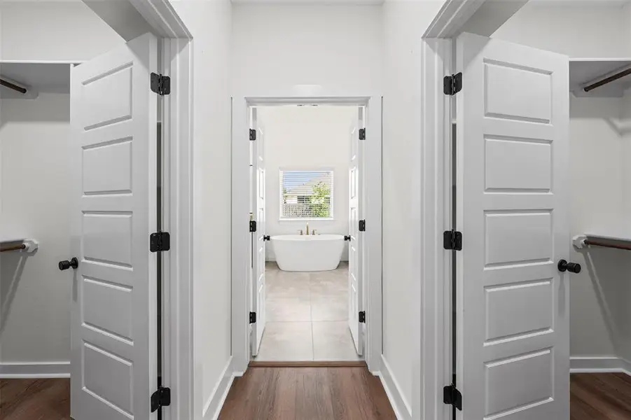 Hallway featuring hardwood floors and white paneled doors leading to a bathroom with a freestanding tub and a window