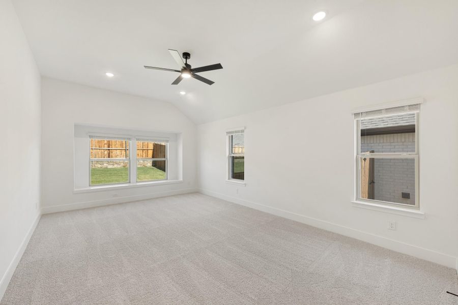 Empty bedroom with vaulted ceiling, ceiling fan, carpet flooring, and three windows