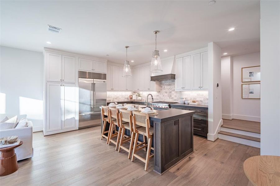 Kitchen with pendant lighting, a breakfast bar area, built in refrigerator, a kitchen island with sink, and white cabinets