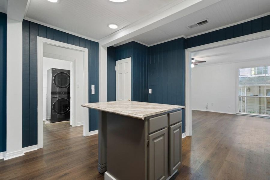 Kitchen with stacked washing machine and dryer, dark wood-style flooring, baseboards, a kitchen island, and ornamental molding