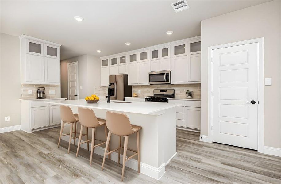 Kitchen featuring a kitchen bar, appliances with stainless steel finishes, a center island with sink, tasteful backsplash, and recessed lighting