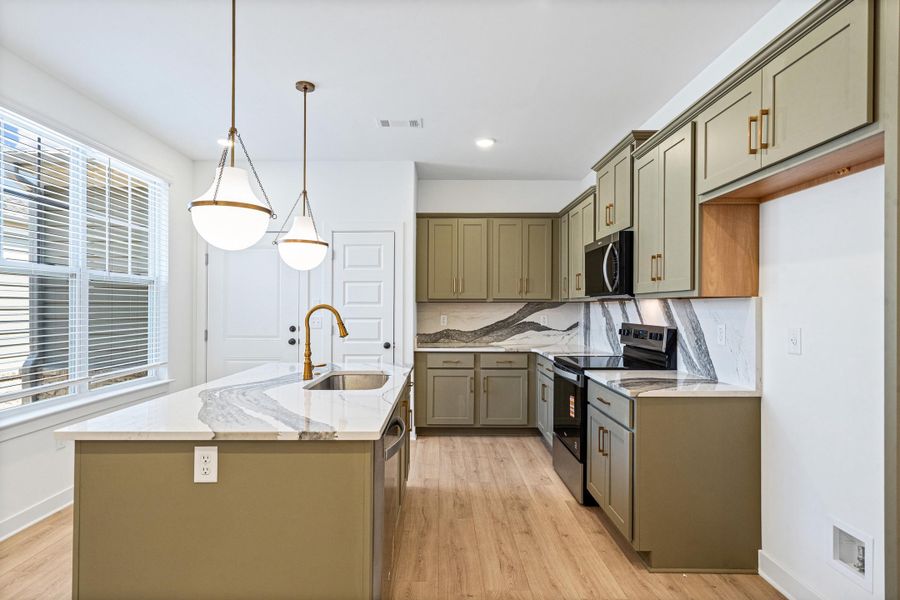 Kitchen featuring a central island with a sink and brass faucet, white countertops with gray veining, olive green cabinetry, and wood-finish flooring Kitchen featuring a central island with a sink and brass faucet, white countertops with gray veining, olive green cabinetry, and wood-finish flooring