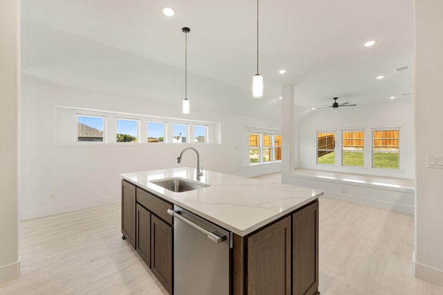 Kitchen island with dark wood cabinets, quartz countertop, and sink open to living area with vaulted ceiling