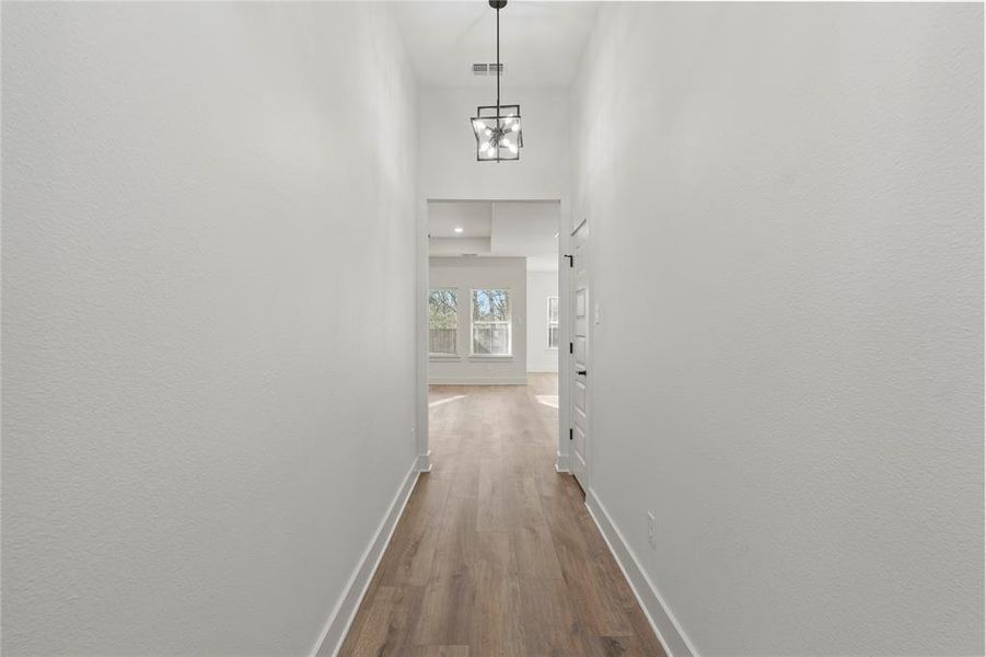 Hall featuring visible vents, baseboards, a towering ceiling, dark wood-type flooring, and a notable chandelier