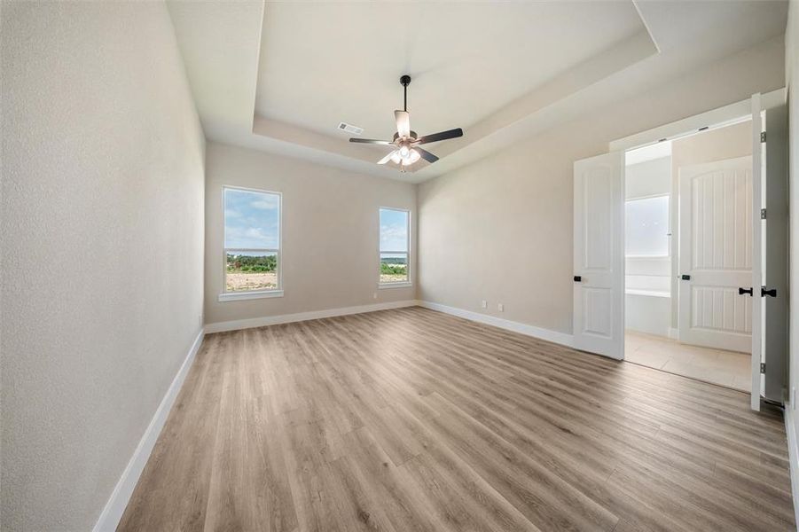 Unfurnished room featuring a tray ceiling, light wood-type flooring, and a ceiling fan Unfurnished room featuring a tray ceiling, light wood-type flooring, and a ceiling fan