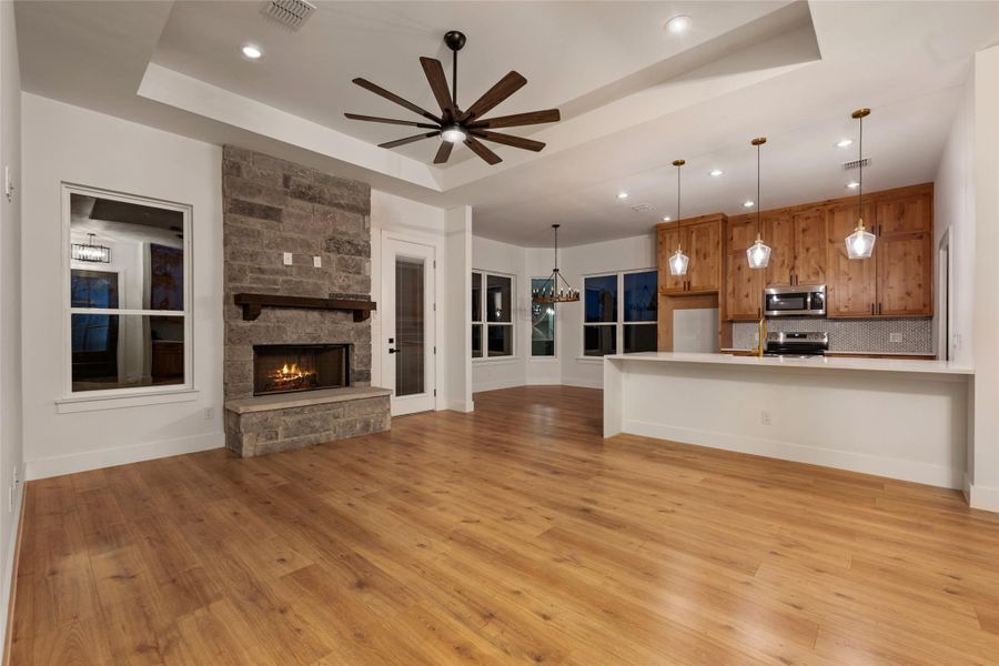Unfurnished living room featuring light wood-style flooring, a fireplace, a tray ceiling, ceiling fan, and recessed lighting