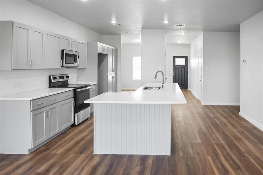 Kitchen with gray cabinets, sink, stainless steel appliances, dark wood-type flooring, and a center island with sink