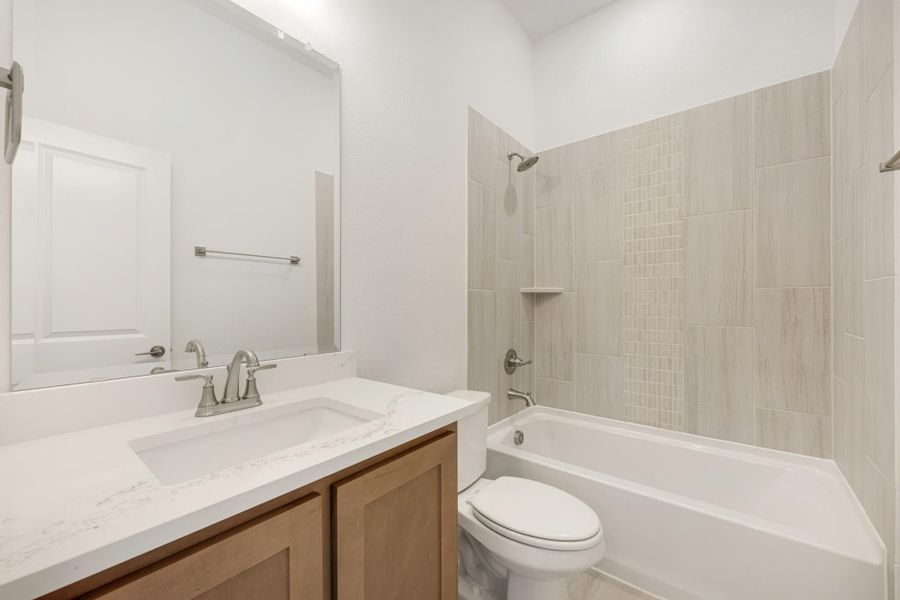 Bathroom with quartz vanity, wood cabinets, and tiled shower-tub combo with brushed nickel fixtures