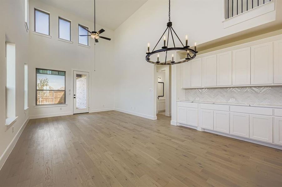 Unfurnished dining area featuring a towering ceiling, light wood finished floors, a chandelier, and ceiling fan
