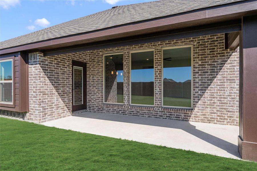 Brick home exterior with covered patio, large windows, and green backyard lawn Brick home exterior with covered patio, large windows, and green backyard lawn