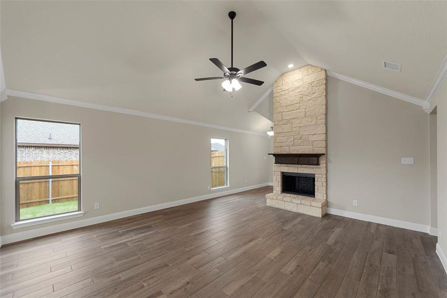 Spacious living area featuring a vaulted ceiling with a ceiling fan, a stone-clad fireplace with a dark wood mantel, large windows, and wood-finish flooring