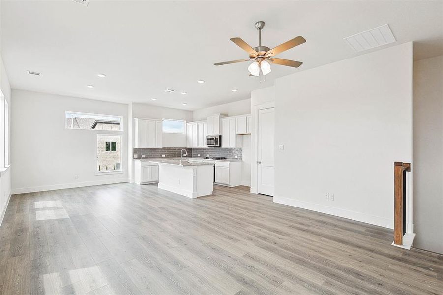 Unfurnished living room with sink, ceiling fan, and light wood-type flooring