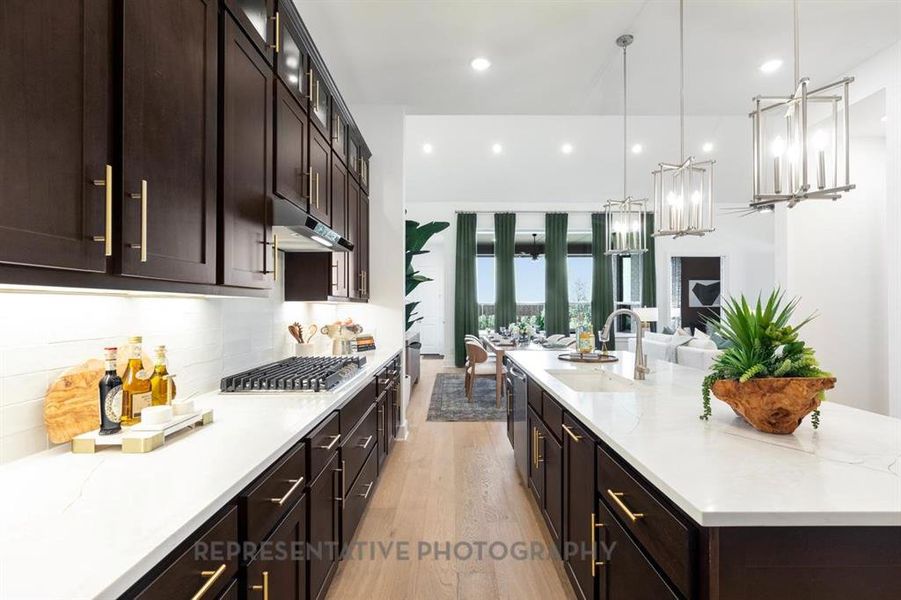 Kitchen with dark brown cabinetry, light wood-style flooring, hanging light fixtures, light stone countertops, and backsplash