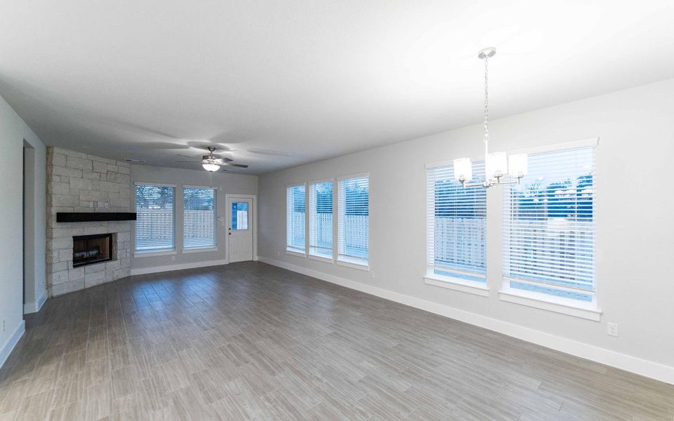 Unfurnished living room featuring ceiling fan with notable chandelier, a stone fireplace, wood finished floors, and baseboards