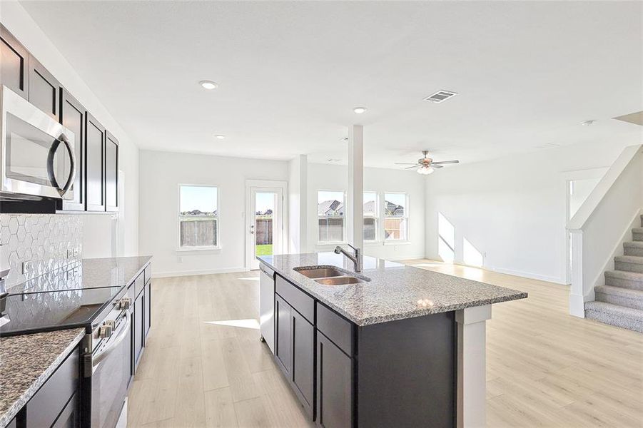 Kitchen with appliances with stainless steel finishes, light hardwood / wood-style flooring, a wealth of natural light, a center island with sink, and sink