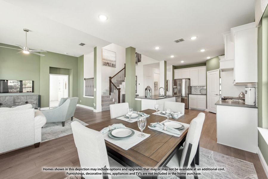 Open-concept dining area with wood table, white chairs, and kitchen visible in background with green accent walls and hardwood floors Open-concept dining area with wood table, white chairs, and kitchen visible in background with green accent walls and hardwood floors