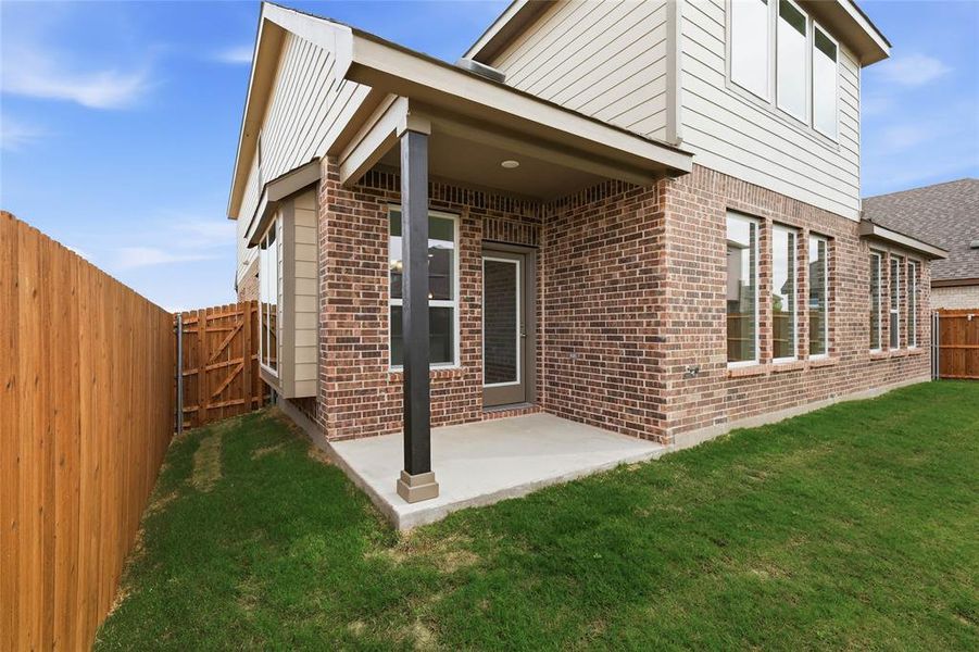 Brick exterior featuring a covered patio with concrete flooring, multiple window installations, and a privacy fence