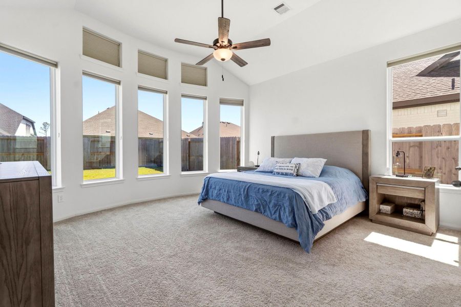 This spacious bedroom features large windows for abundant natural light, a vaulted ceiling with a fan, and neutral carpeting. Perfect for creating a serene retreat.