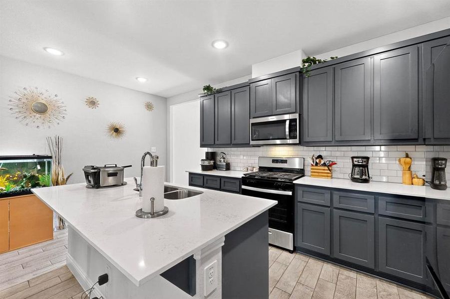 Kitchen featuring light stone counters, appliances with stainless steel finishes, wood tiled floors, a kitchen island with sink, and recessed lighting Kitchen featuring light stone counters, appliances with stainless steel finishes, wood tiled floors, a kitchen island with sink, and recessed lighting