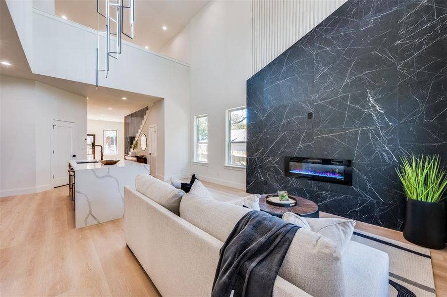 Living room featuring sink, a towering ceiling, tile walls, and light wood-type flooring