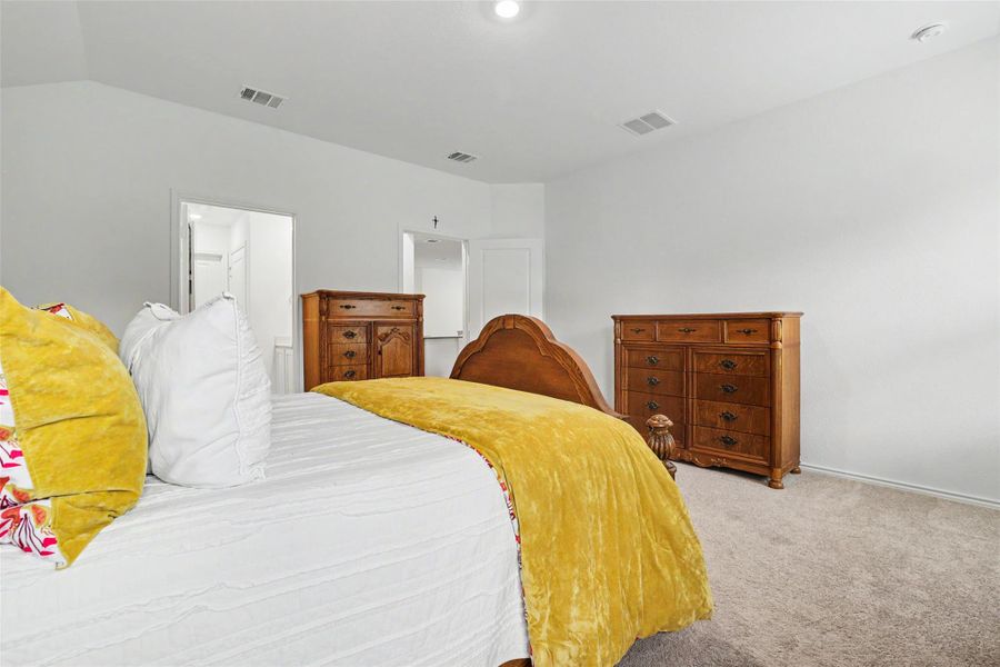 Spacious bedroom featuring light neutral wall paint, carpet flooring, a vaulted ceiling with recessed lighting, and a doorway leading to another room
