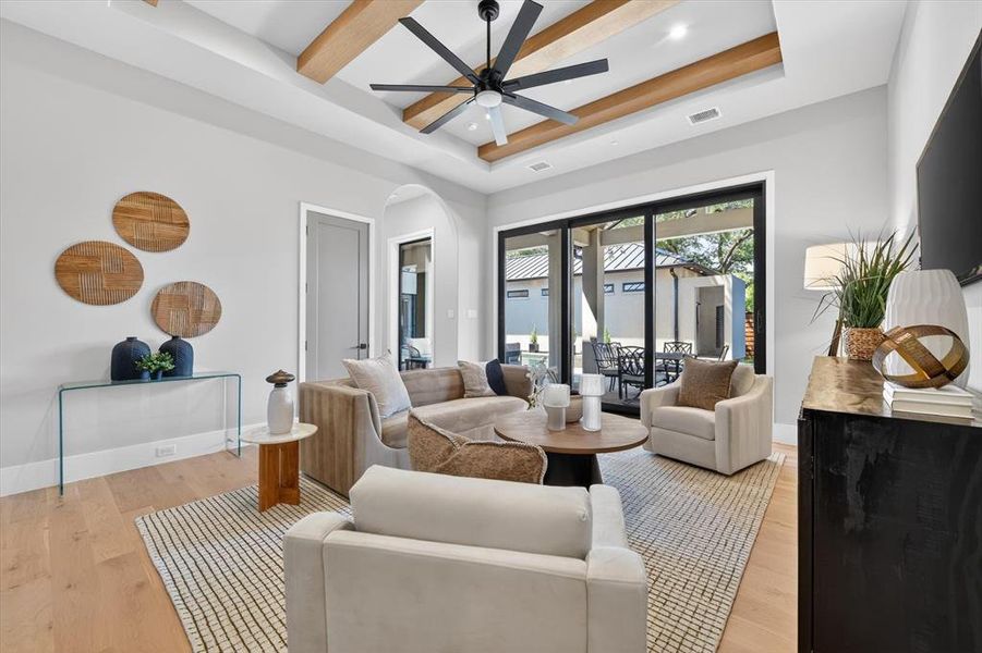 Living area featuring wood-finish flooring, a tray ceiling with exposed wood beams, and a modern ceiling fan Living area featuring wood-finish flooring, a tray ceiling with exposed wood beams, and a modern ceiling fan