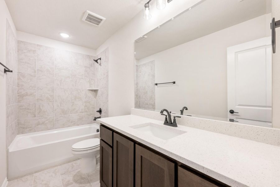 Bathroom with dark wood vanity, white quartz countertop, tiled tub-shower combo, and large mirror