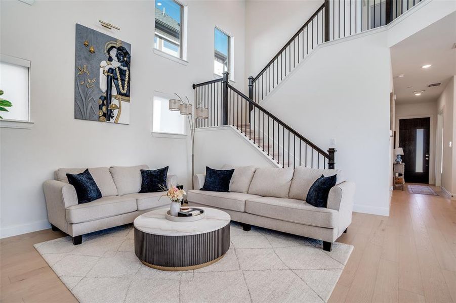 Living area with light wood finished floors, healthy amount of natural light, a high ceiling, and recessed lighting