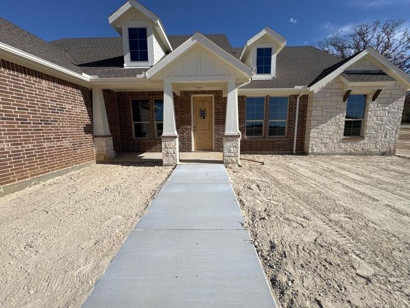 View of front of home with covered porch, roof with shingles, stone siding, and brick siding