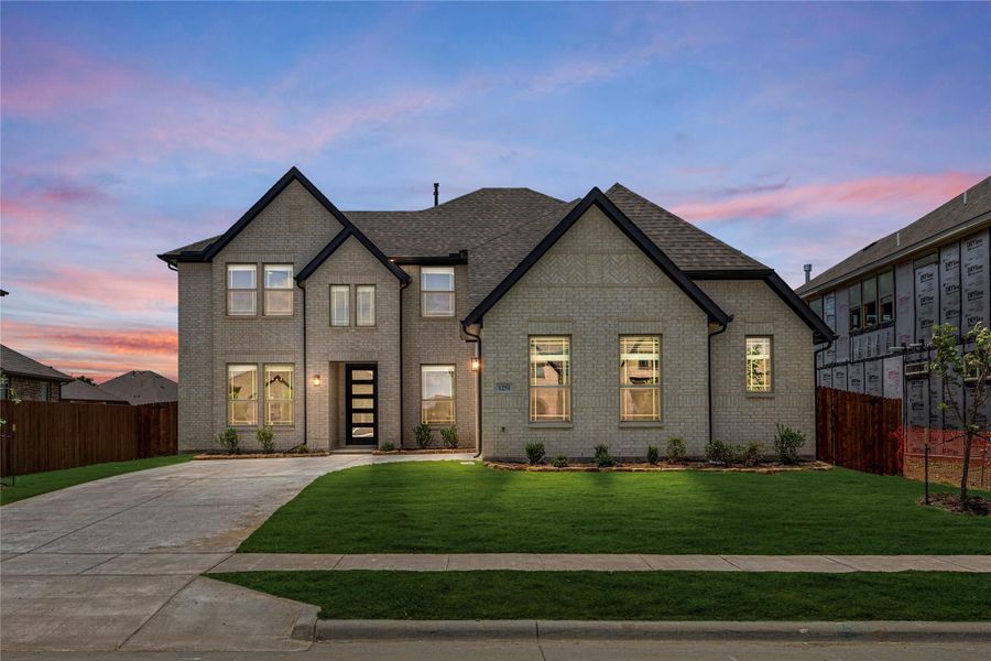 Two-story brick home with dark trim, modern front door, and manicured lawn at dusk