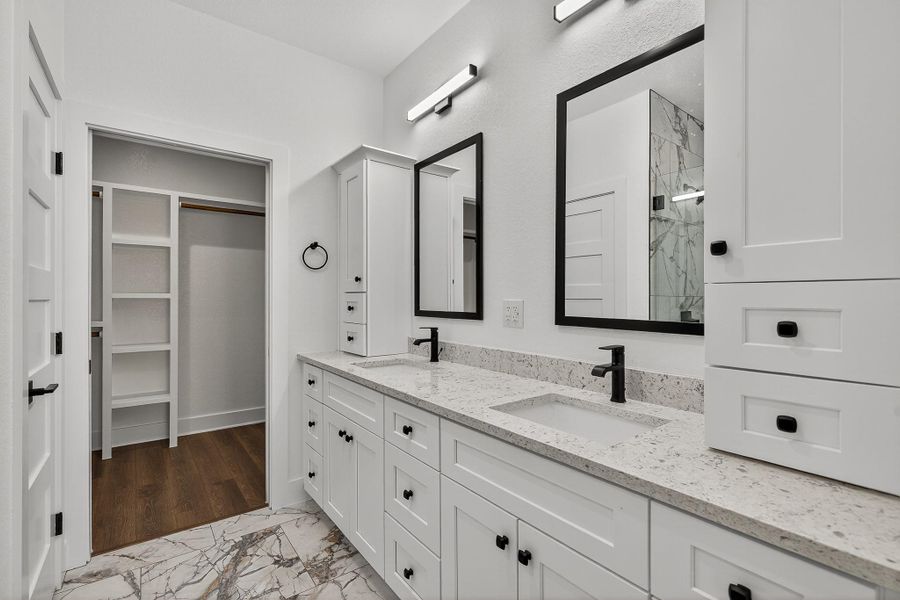Full bath with light marble finish flooring, double vanity, a marble finish shower, and a walk in closet Full bath with light marble finish flooring, double vanity, a marble finish shower, and a walk in closet