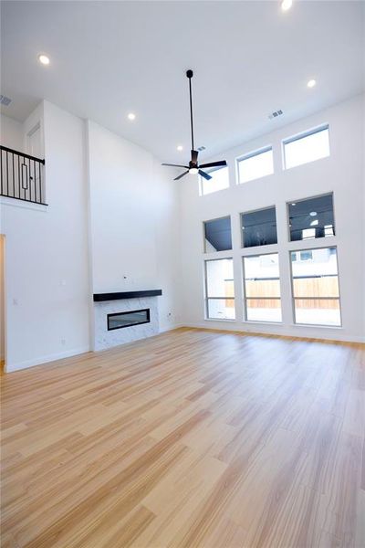 Unfurnished living room featuring light wood-style floors, a high ceiling, a fireplace, recessed lighting, and a ceiling fan Unfurnished living room featuring light wood-style floors, a high ceiling, a fireplace, recessed lighting, and a ceiling fan