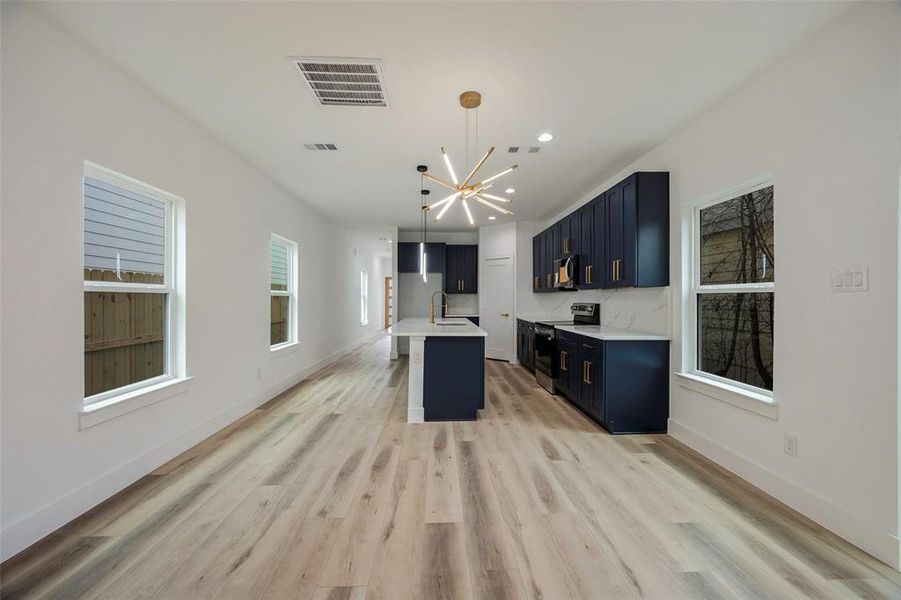 Kitchen with pendant lighting, sink, light hardwood / wood-style flooring, a kitchen island with sink, and stainless steel electric stove