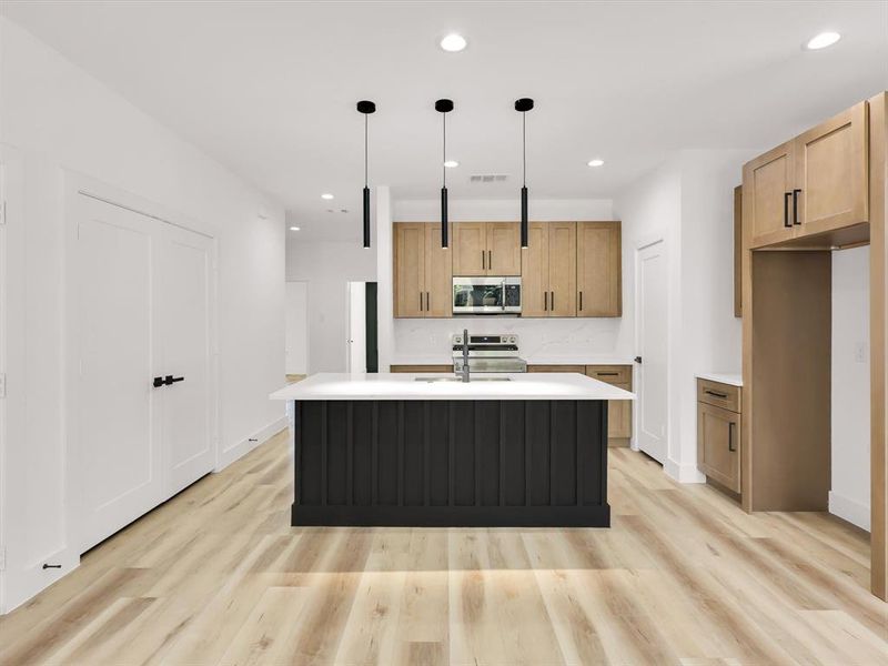 Kitchen featuring hanging light fixtures, light hardwood / wood-style flooring, a center island with sink, and stainless steel appliances