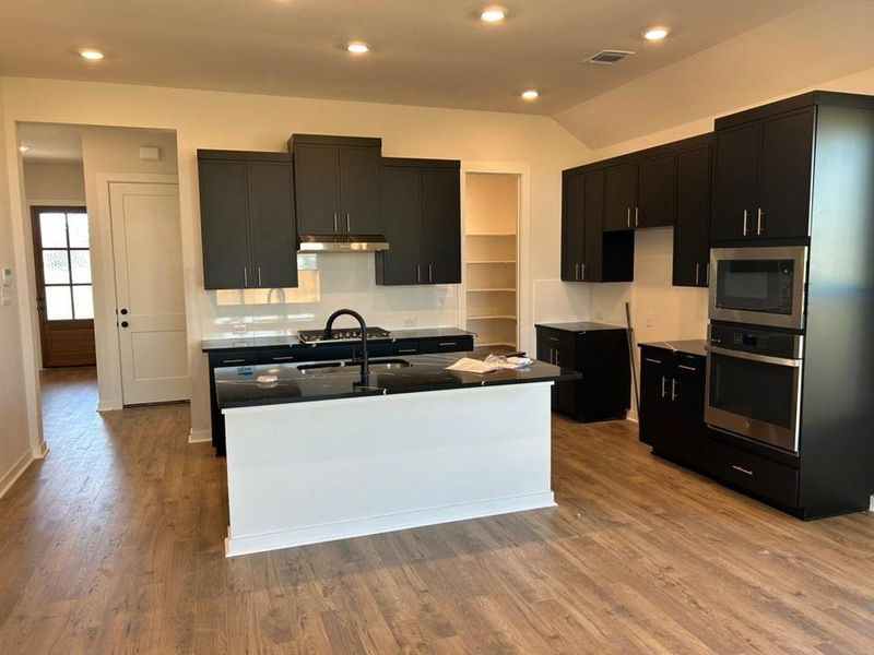 Kitchen with dark cabinetry, a kitchen island with sink, appliances with stainless steel finishes, light wood finished floors, and recessed lighting
