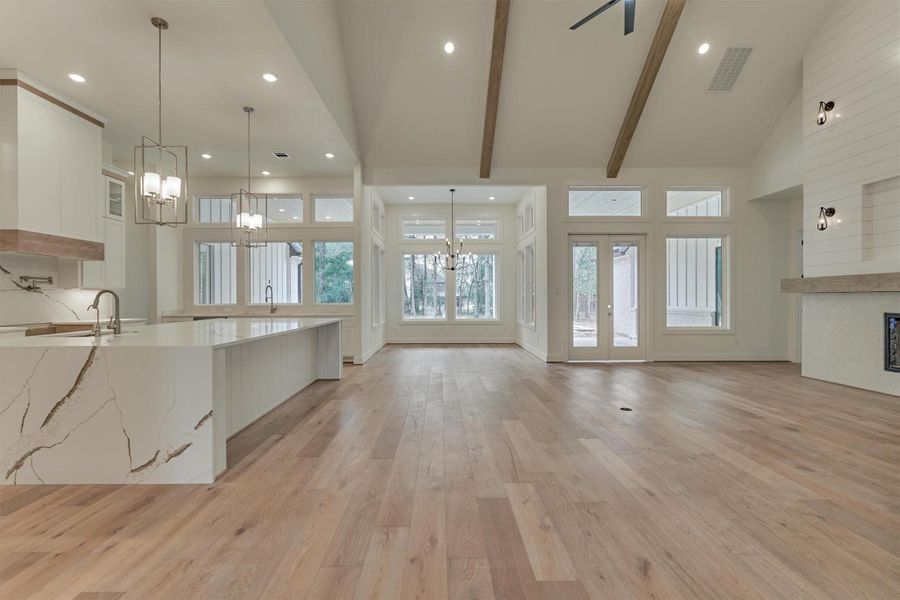 Expansive open-concept living with a stunning waterfall island, floor-to-ceiling windows, and warm wood beams creating a bright, modern, and inviting gathering space.