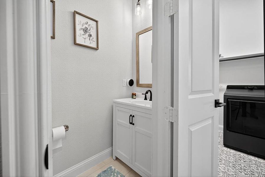 Bathroom vanity with a white countertop and base cabinet, featuring a black faucet and cabinet hardware, illuminated by a modern light fixture