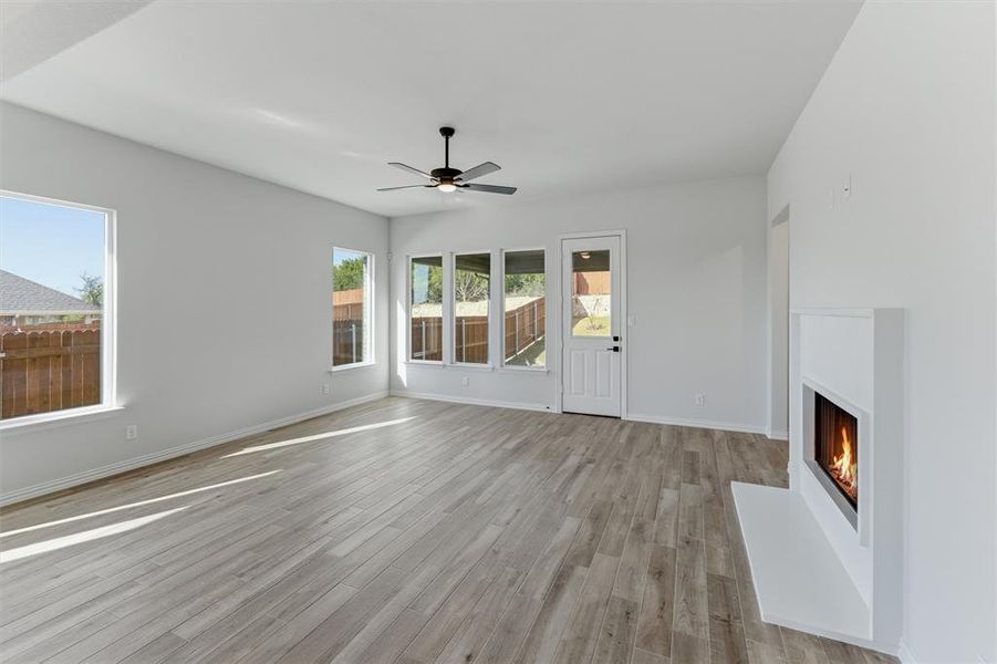 Unfurnished living room featuring a lit fireplace, ceiling fan, and light wood-style flooring