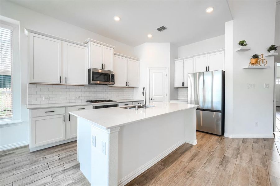 Kitchen with tasteful backsplash, appliances with stainless steel finishes, white cabinetry, light wood-style floors, and recessed lighting Kitchen with tasteful backsplash, appliances with stainless steel finishes, white cabinetry, light wood-style floors, and recessed lighting