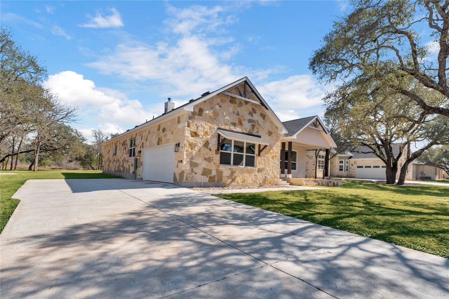 View of front of property with stone siding, a front yard, a porch, concrete driveway, and an attached garage