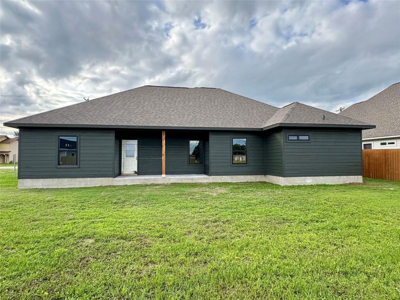 Rear exterior featuring dark horizontal siding, a covered patio area with entry door, and multiple black-framed windows