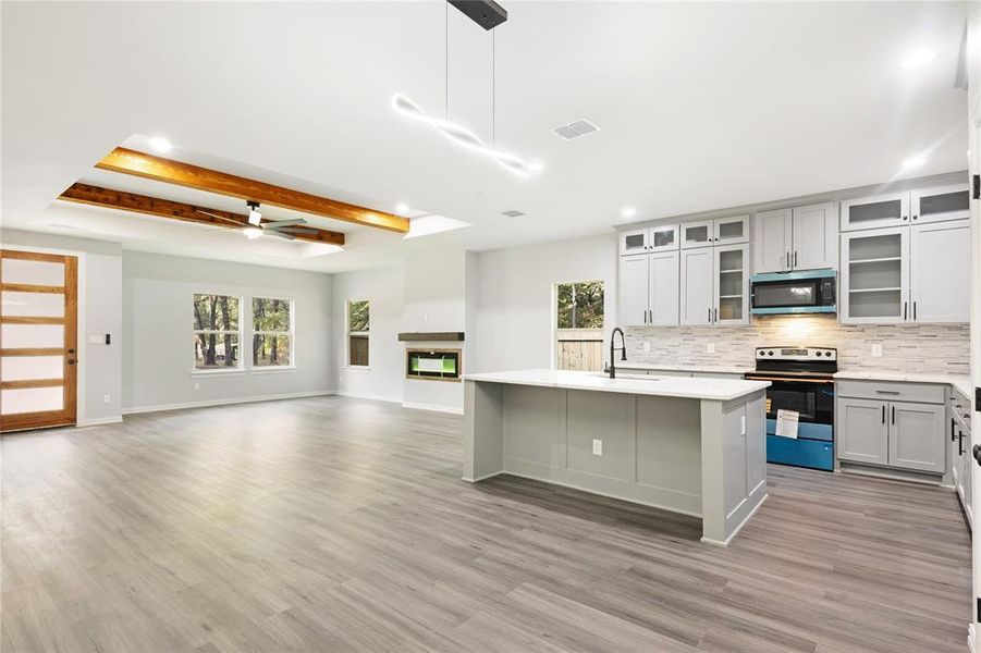 Kitchen with a tray ceiling, range with electric cooktop, a ceiling fan, a kitchen island with sink, and beamed ceiling