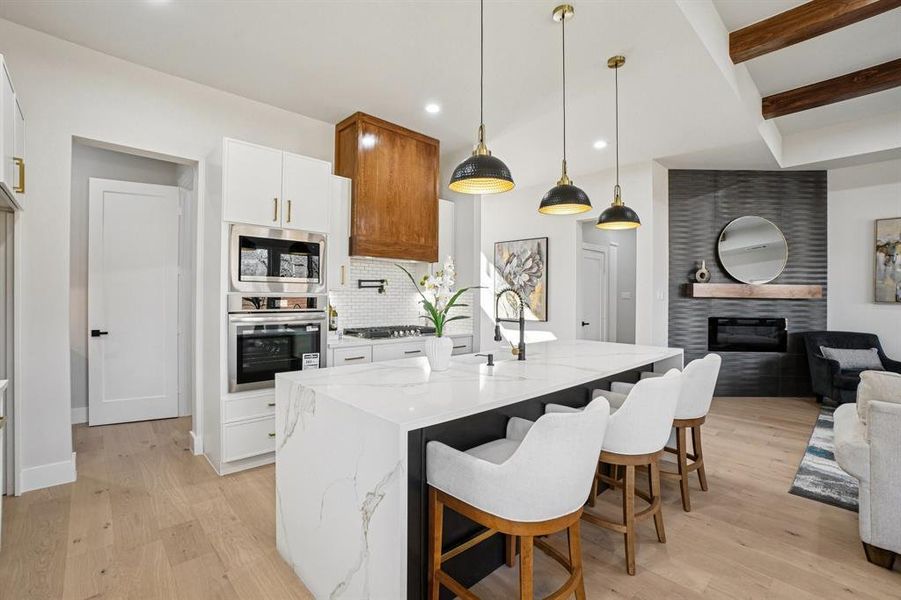 Kitchen featuring beam ceiling, open floor plan, light stone countertops, a tiled fireplace, and decorative light fixtures