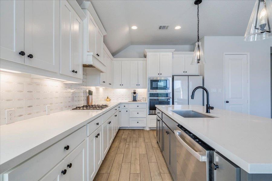 Dual tone kitchen with stainless steel appliances, tasteful backsplash, light wood-style floors, a kitchen island with sink, and dual tone cabinetry