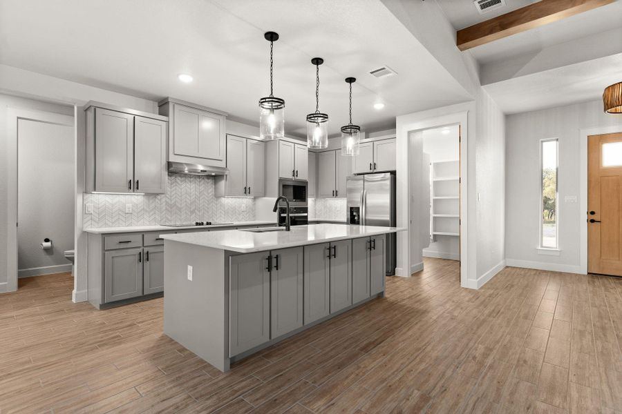 Kitchen featuring gray cabinetry, an island with sink, backsplash, light wood finished floors, and beamed ceiling Kitchen featuring gray cabinetry, an island with sink, backsplash, light wood finished floors, and beamed ceiling