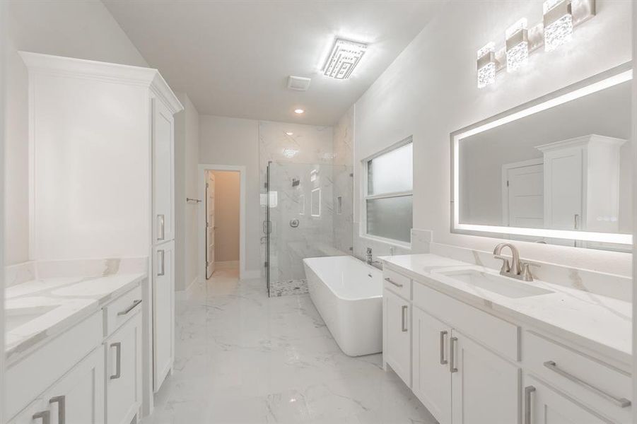 Bathroom featuring a marble finish shower, two vanities, light marble finish floors, and a freestanding tub