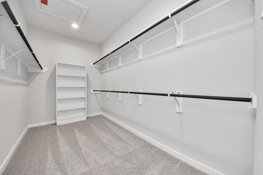 Walk-in closet that epitomizes luxury and practicality. This generously sized space features built-in shelving, offering abundant room for impeccable organization. High ceilings and recessed lighting create a bright and welcoming ambiance. Sample photo of completed home with similar floor plan. Actual colors and selections may vary.
