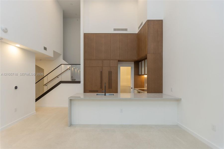 Kitchen featuring floor-to-ceiling wood-finish cabinetry, stone-surfaced waterfall island with integrated sink, and matte black hardware