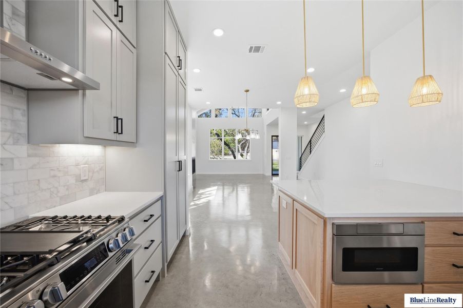 Kitchen with stainless steel appliances, concrete flooring, open floor plan, pendant lighting, and backsplash